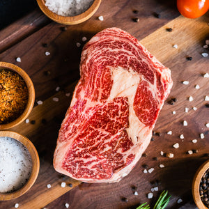 Raw Wagyu ribeye steak with rich marbling on a wooden board with spices and sea salt