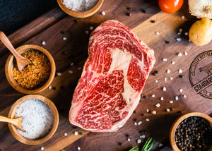 Raw Wagyu ribeye steak with rich marbling on a wooden board with spices and sea salt