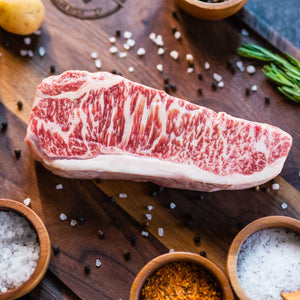 Raw Wagyu NY strip steak on a wooden board with tomatoes and sea salt