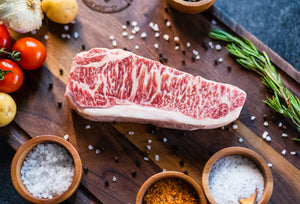Raw Wagyu NY strip steak on a wooden board with tomatoes and sea salt
